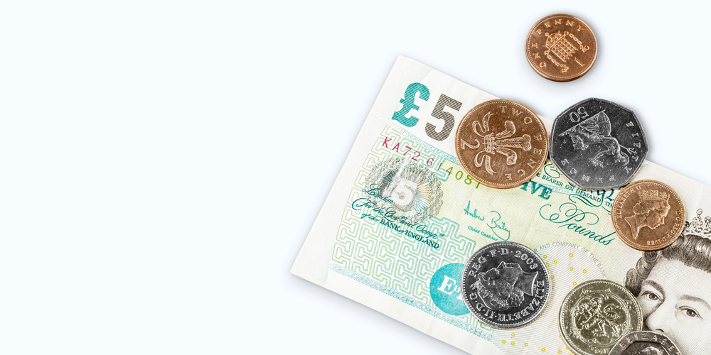 A five-pound British note with several UK coins, including one- and two-pound coins, 50-pence, 10-pence, and a copper penny, arranged on a white background.