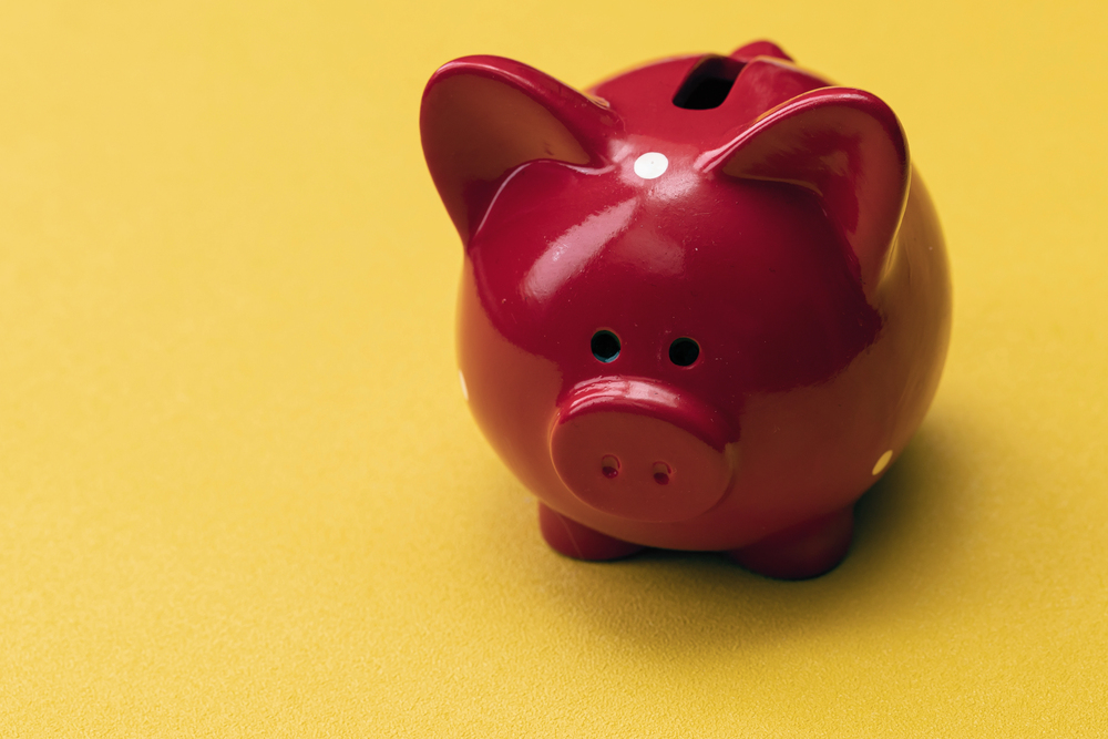 A shiny red piggy bank sits on a smooth yellow surface, slightly angled with its coin slot visible on top.