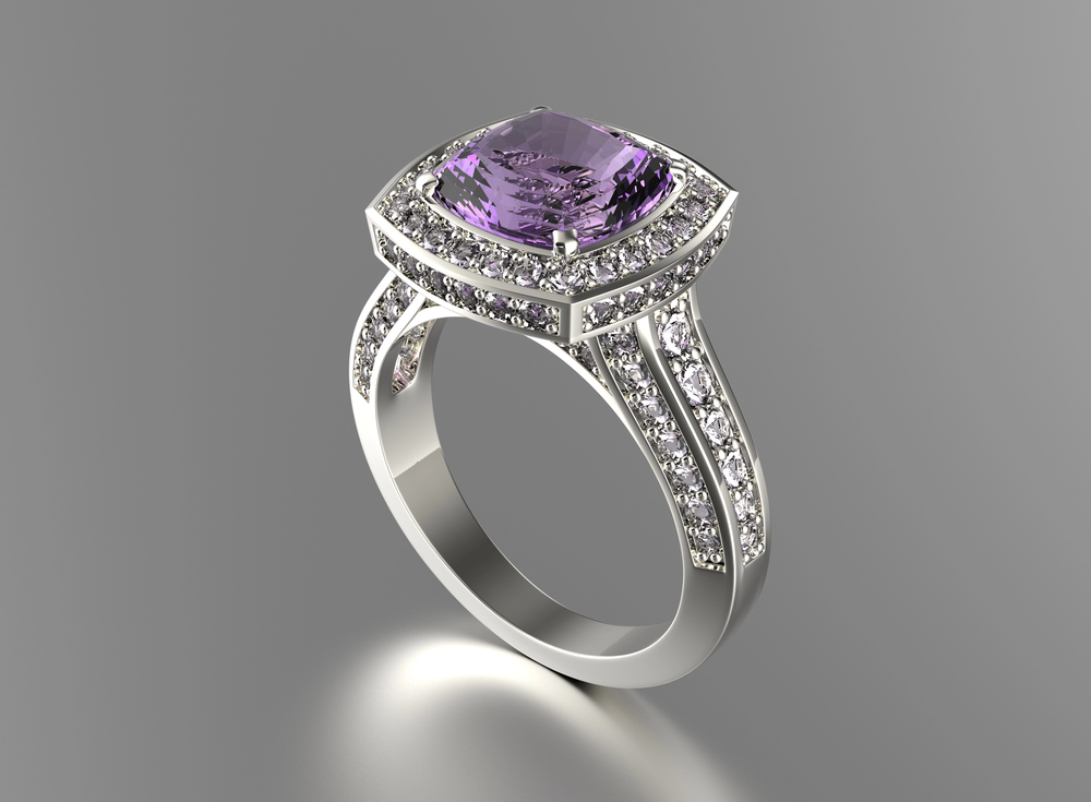 A silver ring with a large, square-cut purple gemstone at the centre, surrounded by small clear stones, sits on a grey background. The band is split and also adorned with small clear stones.