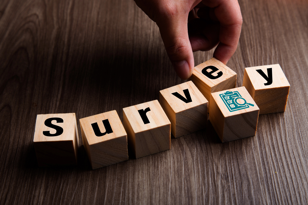 A hand arranges wooden blocks spelling Survey on a wooden surface, with the letter V featuring a small survey icon.
