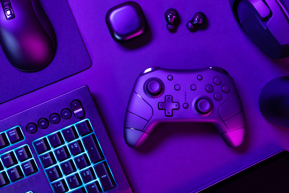 A gaming controller, keyboard, mouse, headset, and earphones sit on a desk, all illuminated by purple and blue neon lighting.