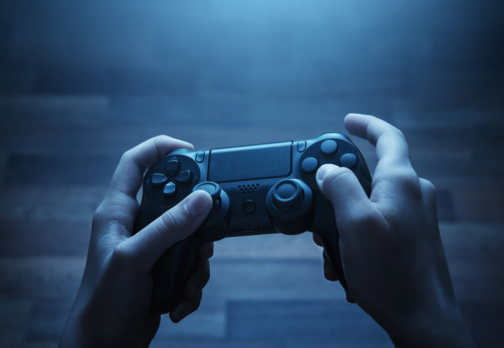 A person holds a black video game controller with both hands against a blurred, blue-lit background, ready to play.