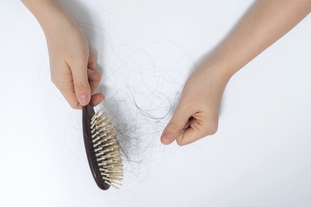 A person holds a hairbrush with one hand and a clump of loose hair with the other on a white background, suggesting hair loss or shedding.