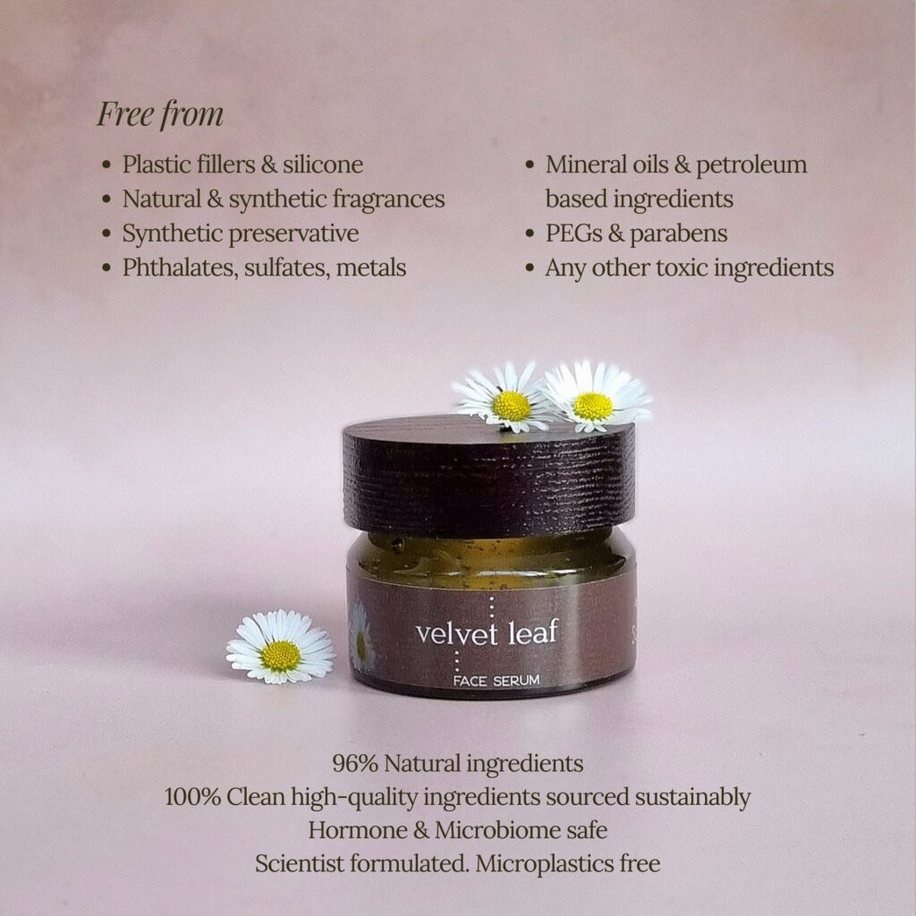 Small glass jar labelled velvet leaf FACE SERUM with white daisies beside and on top. Text lists ingredients the product is free from, and states it contains 96% natural, sustainably sourced ingredients. Pale mauve background.