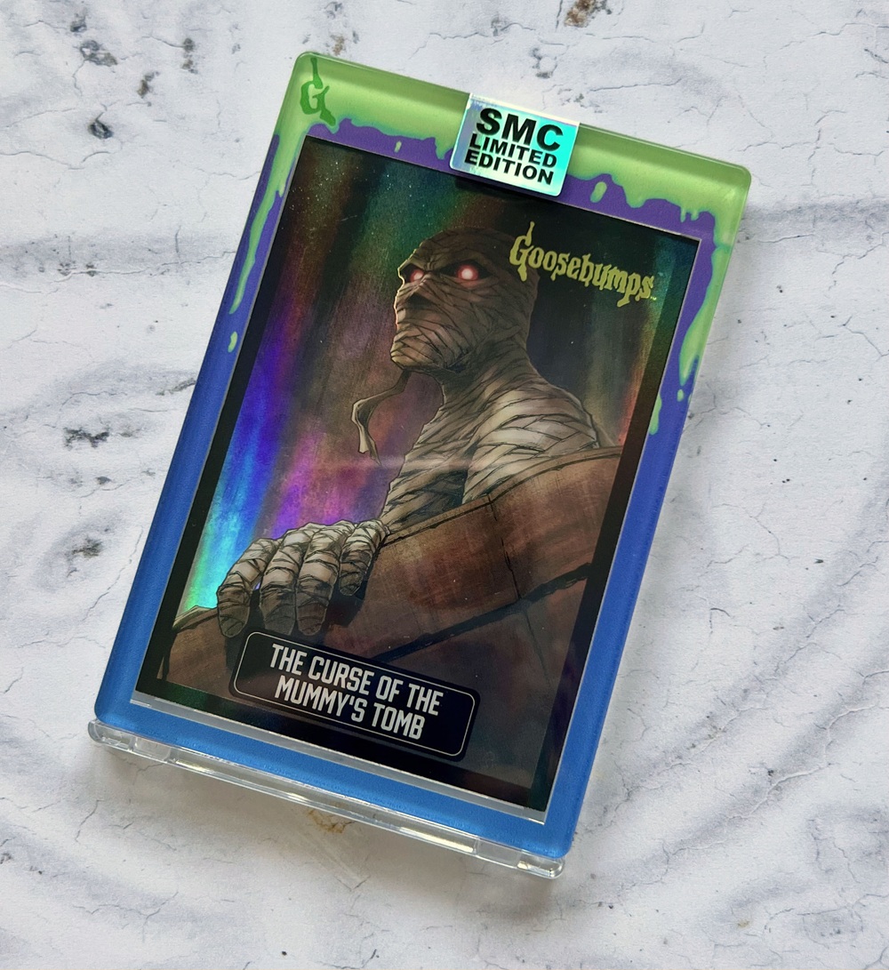 A holographic Goosebumps collectable card features a mummy with red eyes and a wrapped face. The card reads “The Curse of the Mummy’s Tomb” and has a “SMC Limited Edition” label on top.