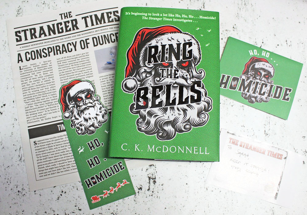 A green book titled Ring the Bells by C.K. McDonnell, featuring a Father Christmas illustration, is surrounded by a newspaper, a postcard, and a bookmark, all with holiday and homicide themes.