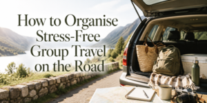 Open car boot packed with bags, a blanket, a map, and a water bottle beside a mountain road and lake. Sunlight highlights a scenic, peaceful landscape. Text reads: “How to Organise Stress-Free Group Travel on the Road.”.