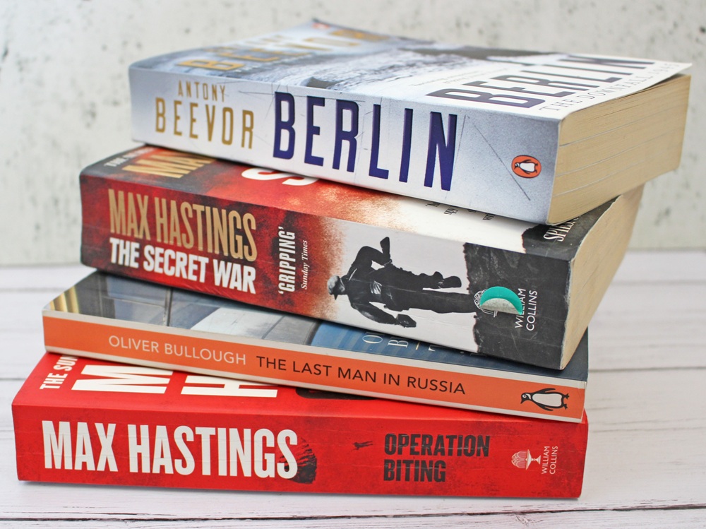 Four books stacked on a white surface: Berlin by Antony Beevor, The Secret War and Operation Biting by Max Hastings, and The Last Man in Russia by Oliver Bullough.