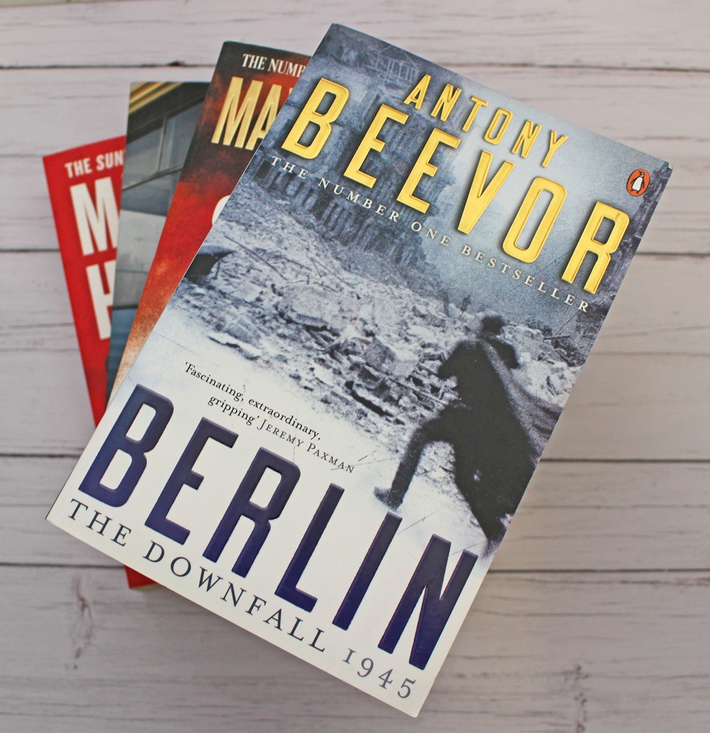 Three books, with Berlin: The Downfall 1945 by Antony Beevor on top, showing a black and white image of a soldier. Other books are stacked underneath on a wooden surface.