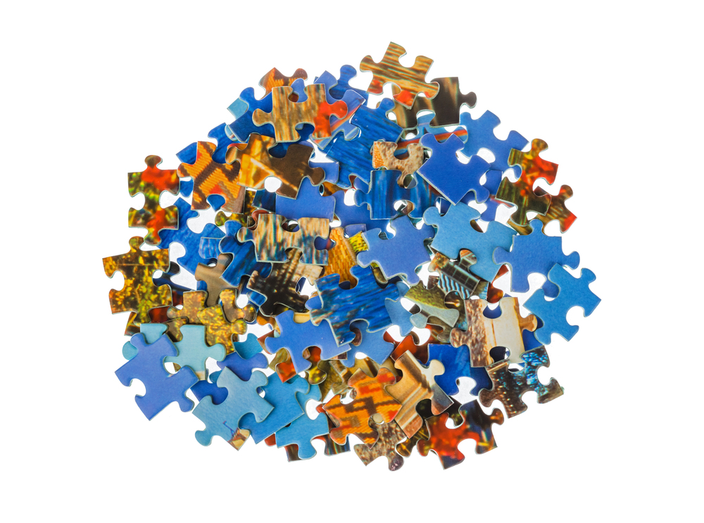 A pile of colourful jigsaw puzzle pieces, mainly blue, scattered on a white background.