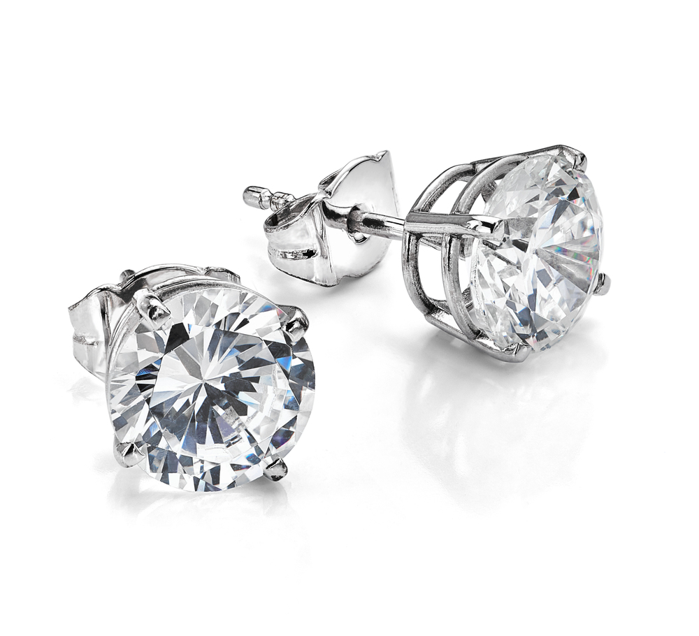 A pair of round, clear diamond stud earrings with silver prong settings and posts, displayed on a white background.