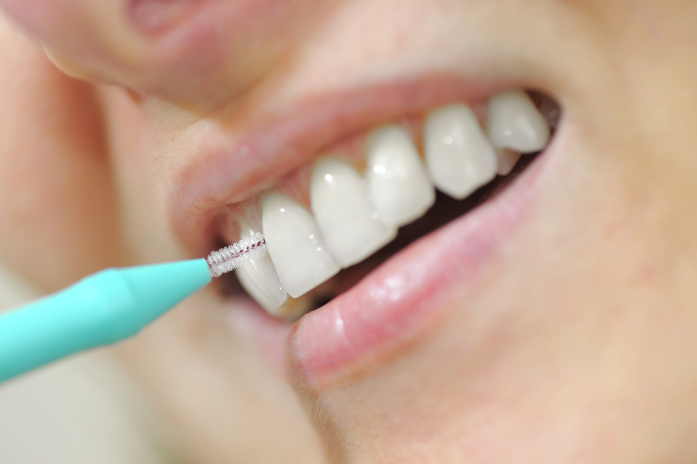 A close-up of a person using an interdental brush to clean between their teeth, showing healthy white teeth and a partial smile.