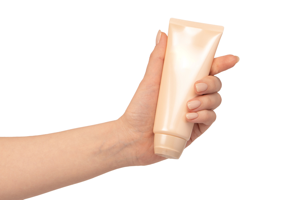 A hand holding a beige, unbranded squeezy tube, likely for lotion or cream, against a white background.