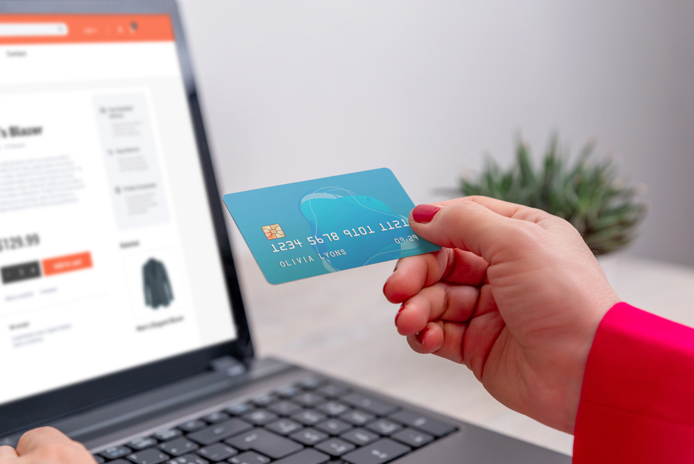 A person holding a blue credit card in front of a laptop displaying an online shopping website, preparing to make a purchase.