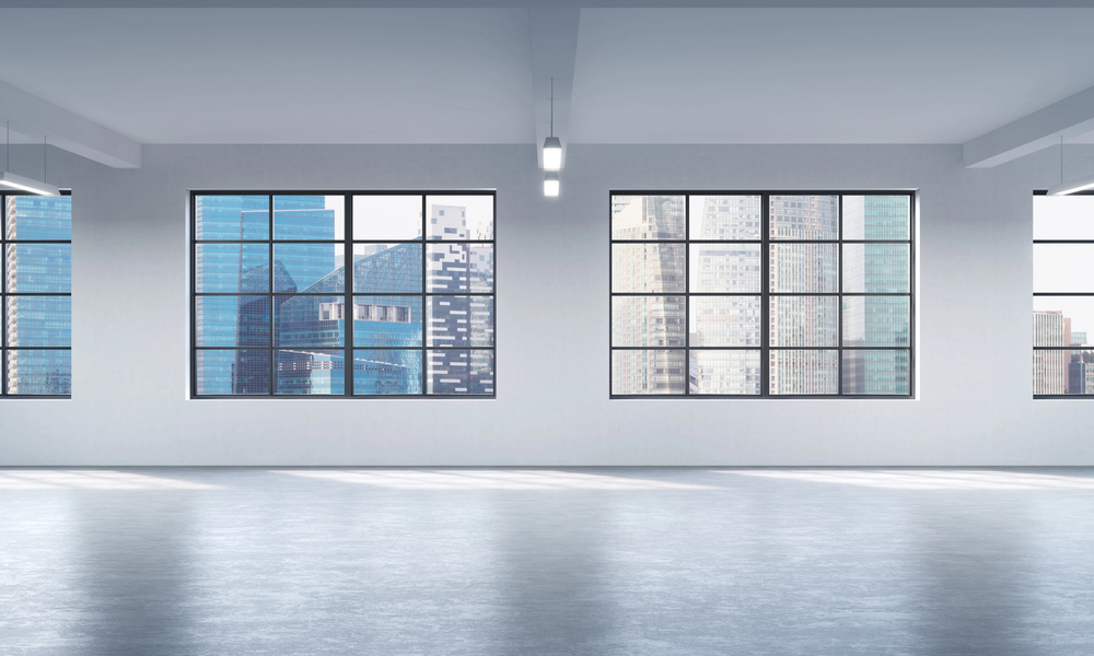 Empty modern room with large windows showing a city skyline with tall glass buildings. Natural light fills the spacious, clean interior with a shiny floor and white walls.