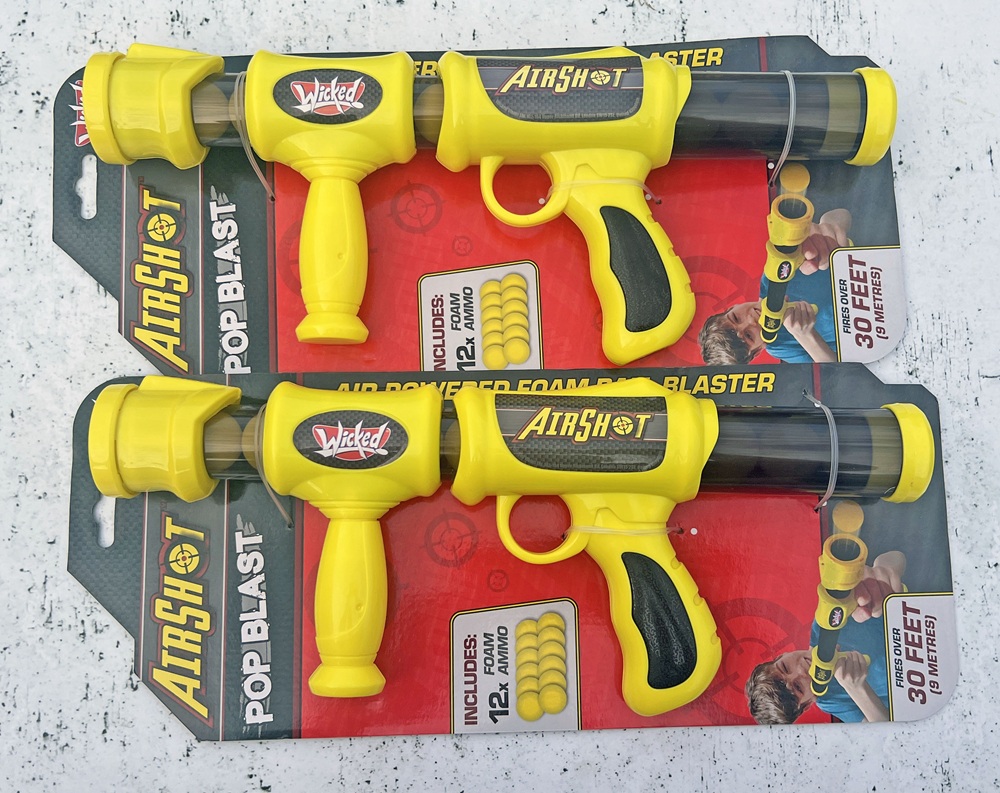 Two yellow AirShot Pop Blast air-powered foam pellet toy blasters are packaged with ammo and labelled for 30 feet range, against a red and grey background.
