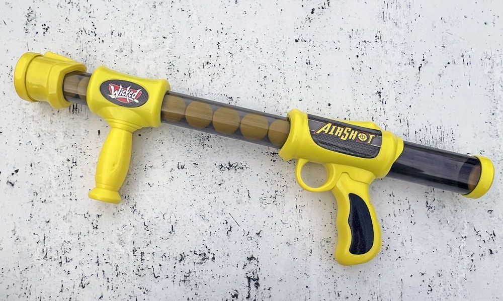 A yellow and black toy air gun labelled Airshot with foam balls inside, lying on a white speckled surface.