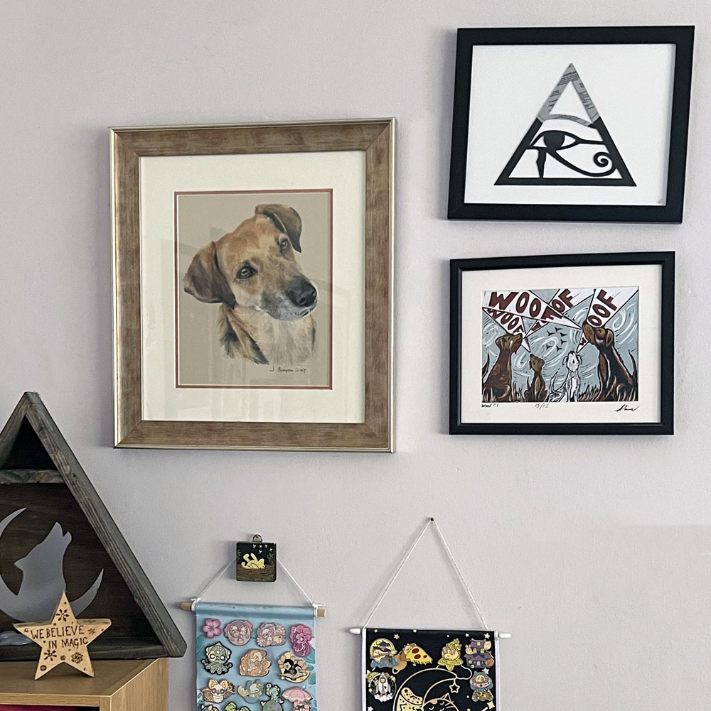 A wall displays framed dog art, an Eye of Horus triangle, a woof woof illustration, a shelf with a star reading We believe in magic, and hanging banners with colourful pins and designs.