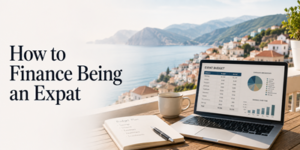 A laptop displaying an event budget chart sits on a table with a notebook, pen, and coffee cup, overlooking a scenic coastal village. Text reads: How to Finance Being an Expat..
