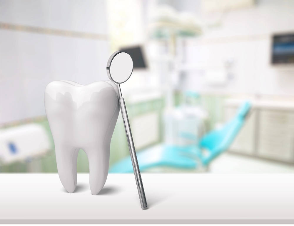 A large tooth model and a dental mirror are displayed on a counter, with a blurred dental surgery and examination chair in the background.