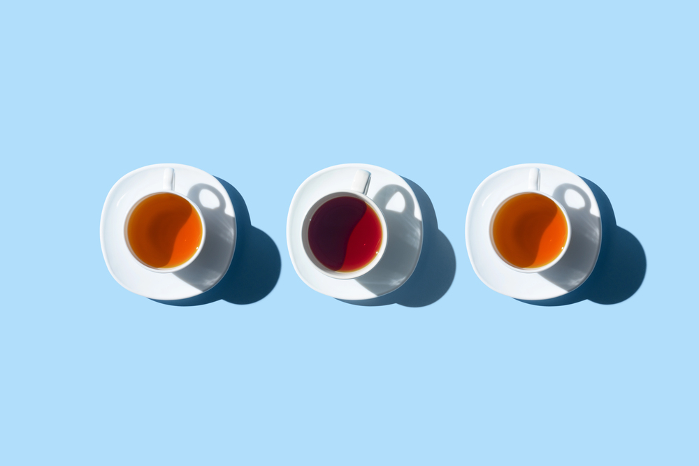 Three white cups filled with different types of tea are arranged in a row on a light blue background, each casting a shadow to the right.