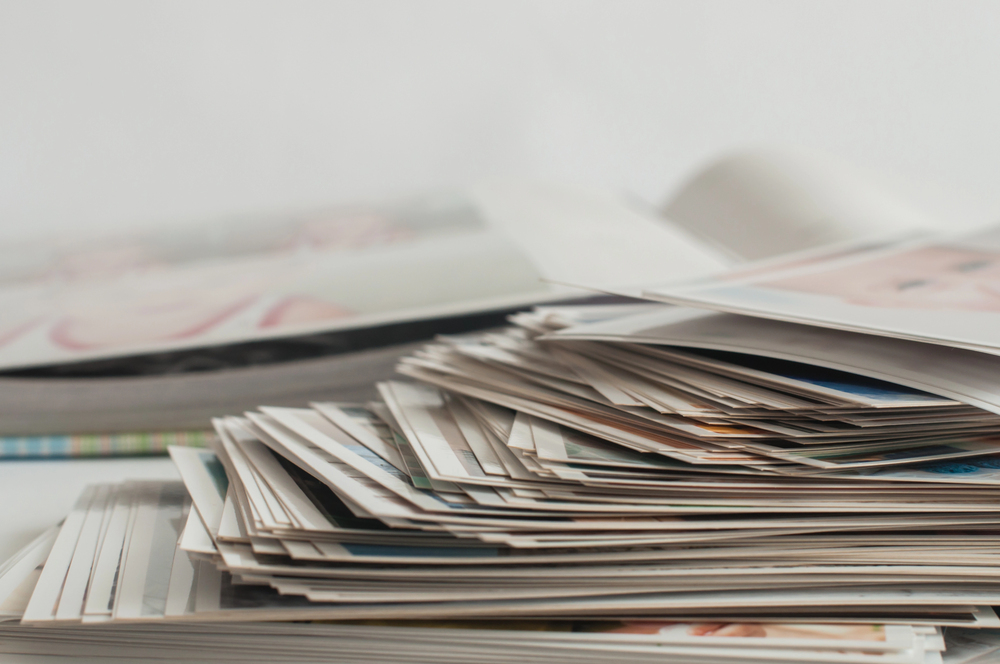 A large stack of printed photographs lies on a white surface with an open photo album in the background, creating a nostalgic and organised scene.