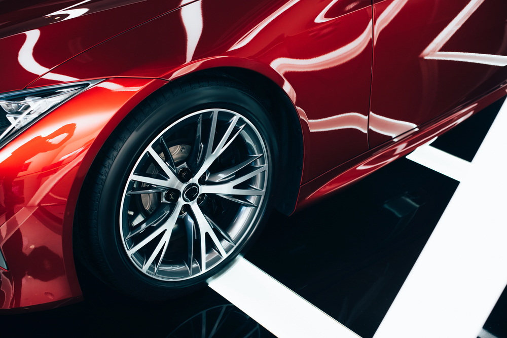 Close-up of a shiny red car's front wheel and sleek body, with dramatic white and black floor reflections accentuating the modern, sporty design.