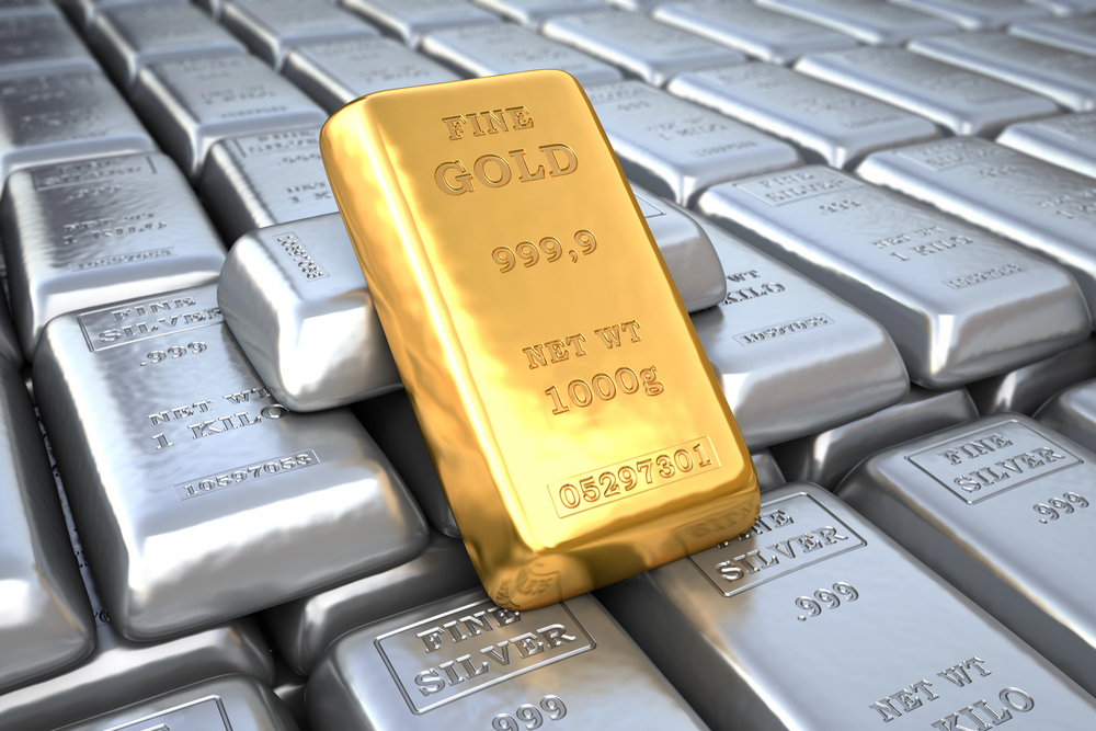 A single gold bar labelled FINE GOLD 999.9 rests on top of several silver bars labelled FINE SILVER 999.0, creating a striking contrast between the two precious metals.