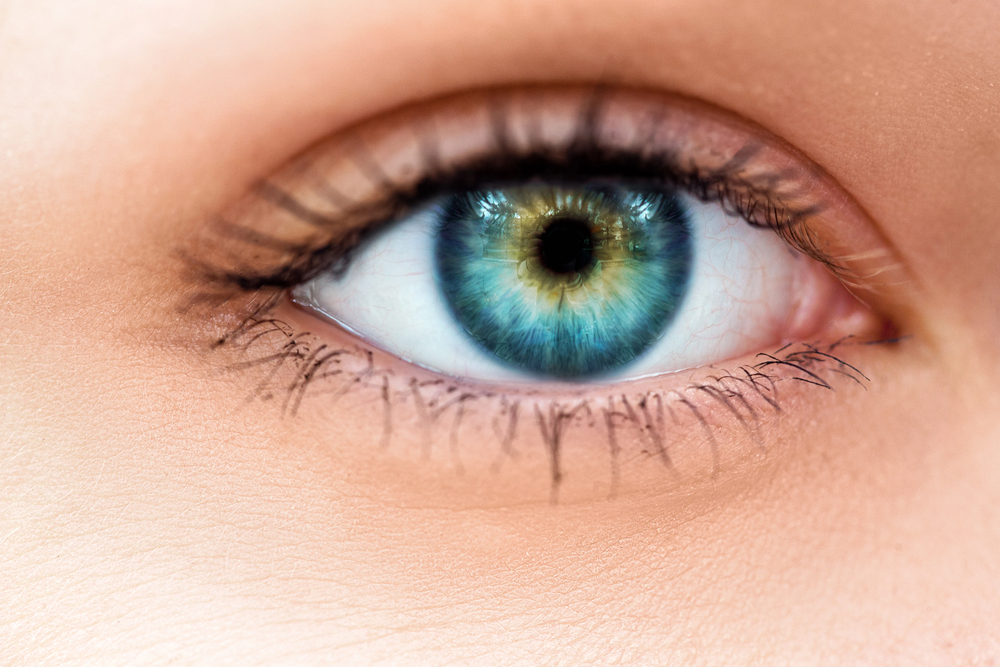 Close-up of a blue-green eye with dark pupil, detailed iris patterns, and long eyelashes, showing the skin around the eye.