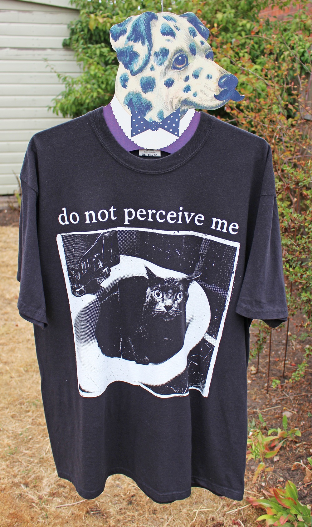 A shirt on a mannequin with a Dalmatian dog head. The shirt reads do not perceive me and shows a black cat sitting in a bathroom sink, looking up.