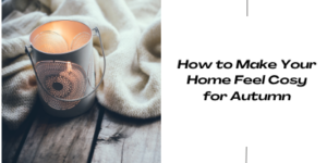 A lit candle in a decorative holder sits on a wooden surface beside a cream blanket. The text reads, How to Make Your Home Feel Cosy for Autumn.