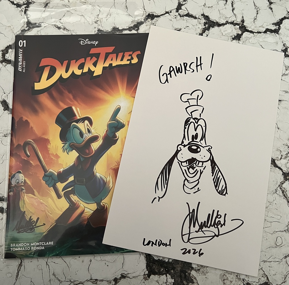 A DuckTales comic book featuring Scrooge McDuck is beside a signed sketch of Goofy saying GAWRSH! The sketch is signed and dated London 2024. Both rest on a marble-patterned surface.