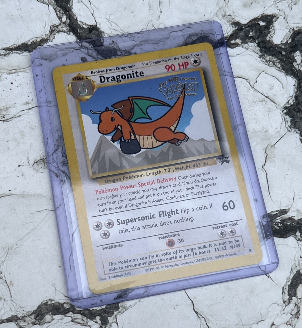 A Special Delivery Dragonite Pokémon card is encased in a protective sleeve and placed on a white, cracked surface. The card features Dragonite carrying a letter with the Pokémon Centre logo.