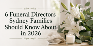 6 Funeral Directors Sydney Families Should Know About in 2026 beside white lilies, a candle, and a folded cloth on a table.