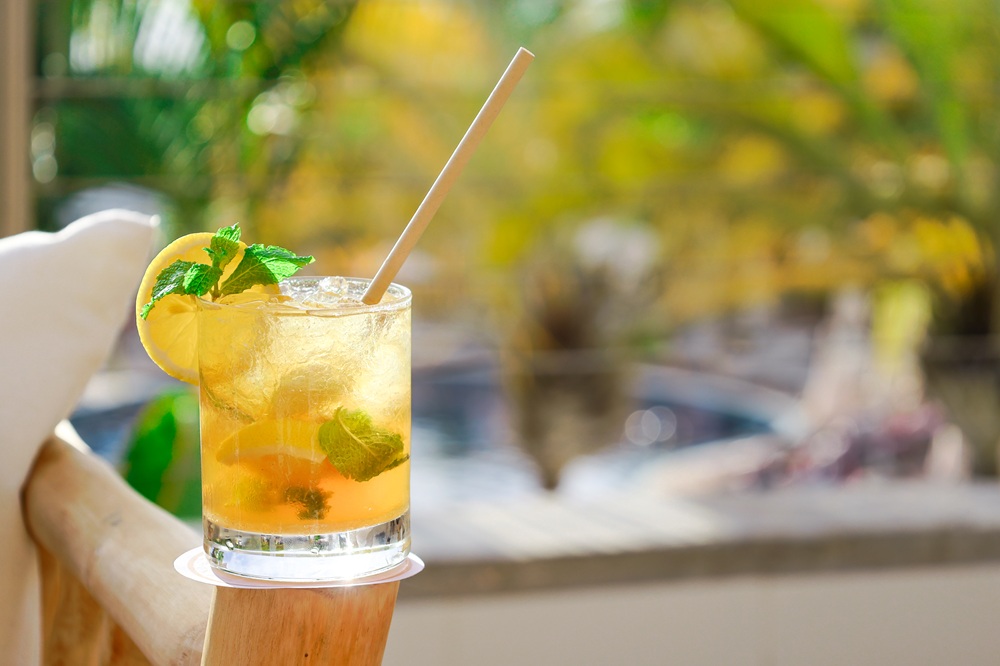 An iced cocktail in a rocks glass garnished with a lemon slice and mint sprigs, with a straw inserted.