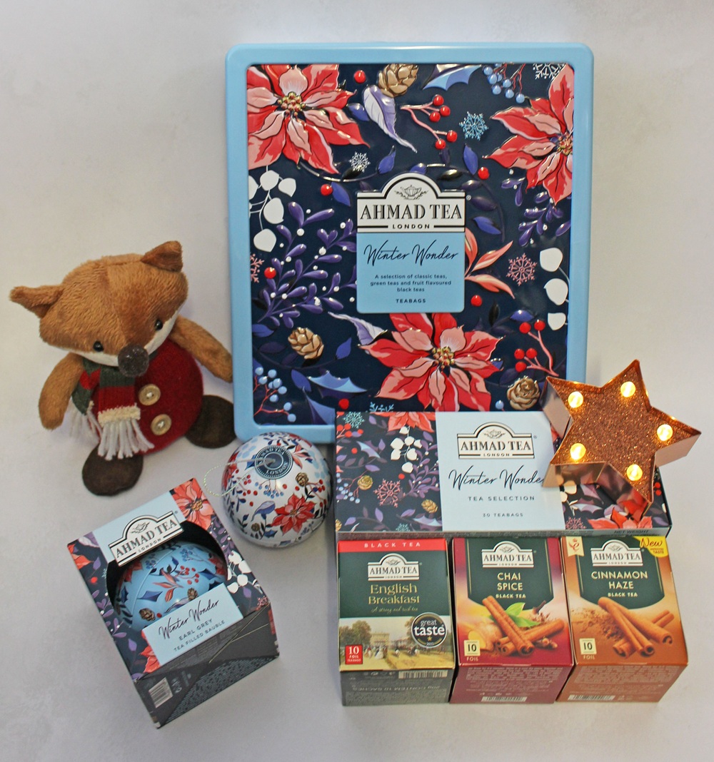 Ahmad Tea winter collection featuring a floral tin, tea boxes in English Breakfast, Chai Spice, and Cinnamon Haze, an Earl Grey tea bauble, a stuffed fox toy, and a light-up star ornament.