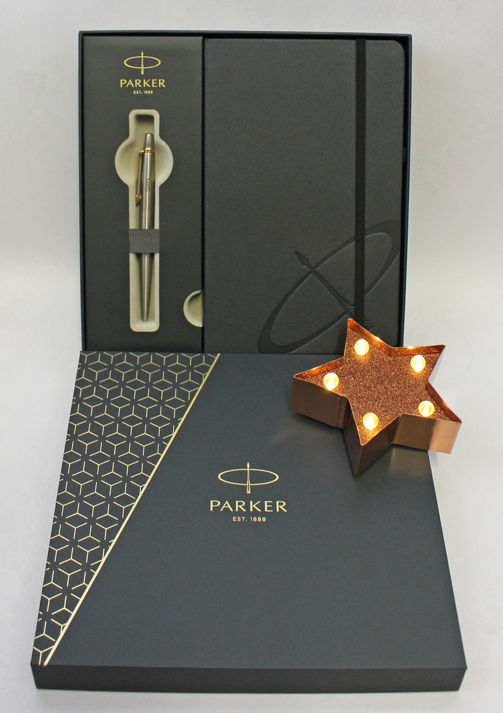 Parker gift set containing a silver pen and a black notebook, displayed in a branded box next to a glowing, star-shaped light.