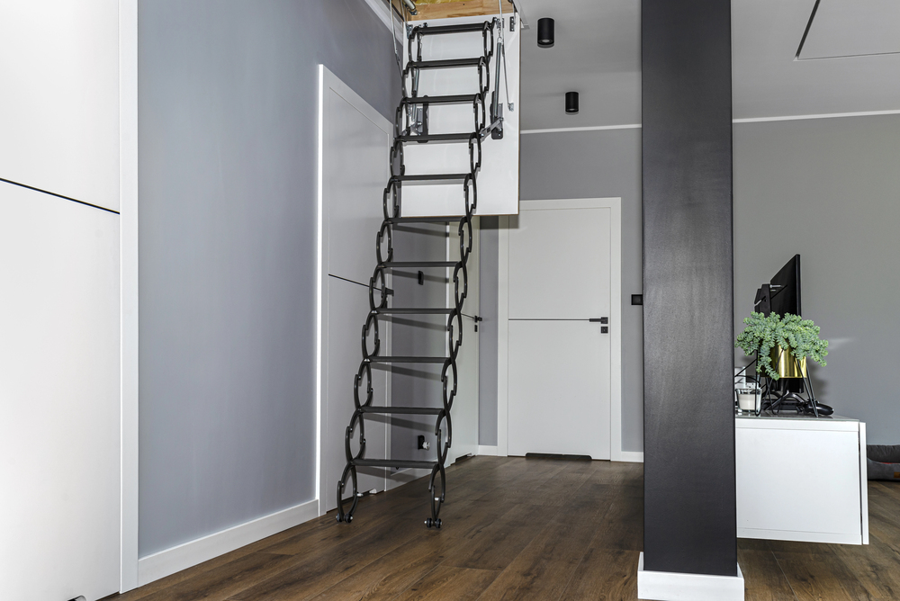 Retractable black metal loft ladder unfolded from the ceiling in a modern corridor.