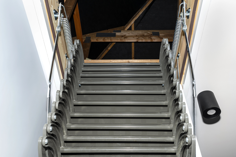 A retractable folding loft ladder viewed from the top of the stairs, leading down into an opening in the ceiling.