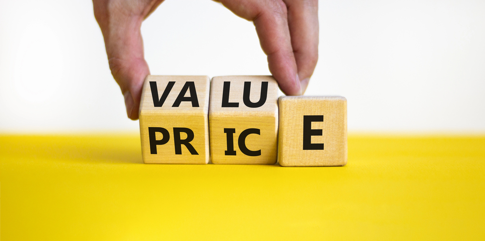 A hand moves wooden blocks to change the word PRICE to VALUE.