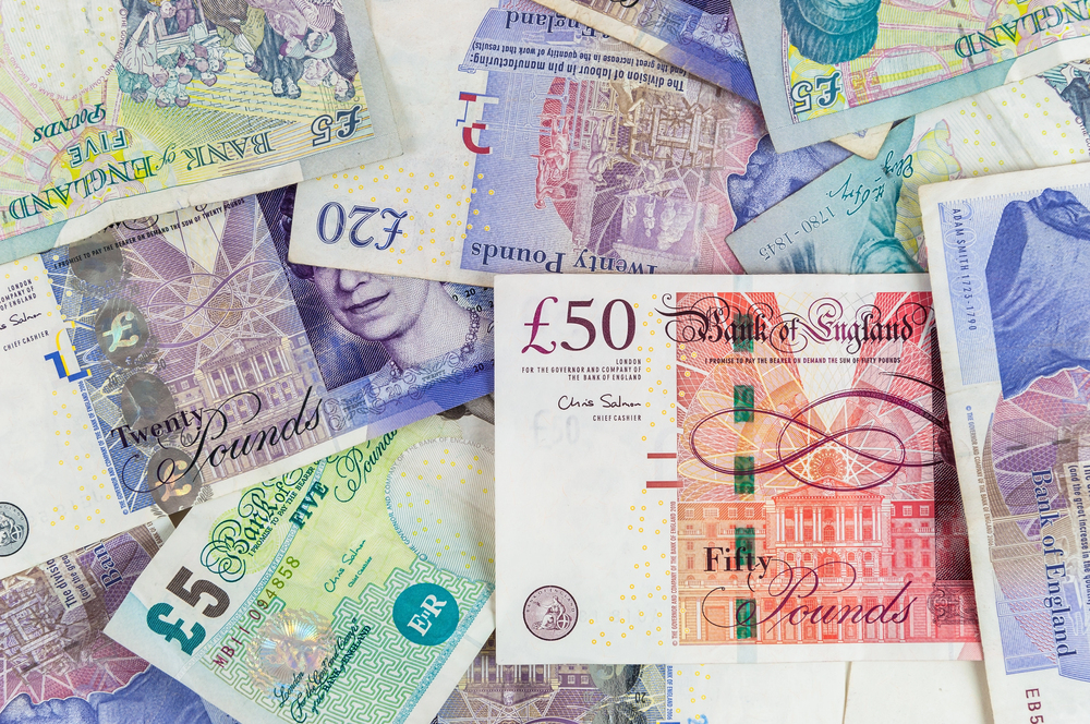 A variety of British pound sterling banknotes, including five, twenty, and fifty-pound denominations, layered together.