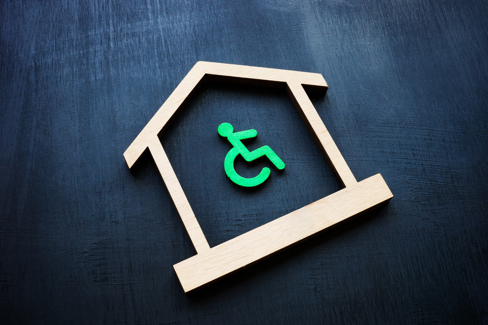 A wooden house outline containing a green wheelchair accessibility symbol on a dark surface.