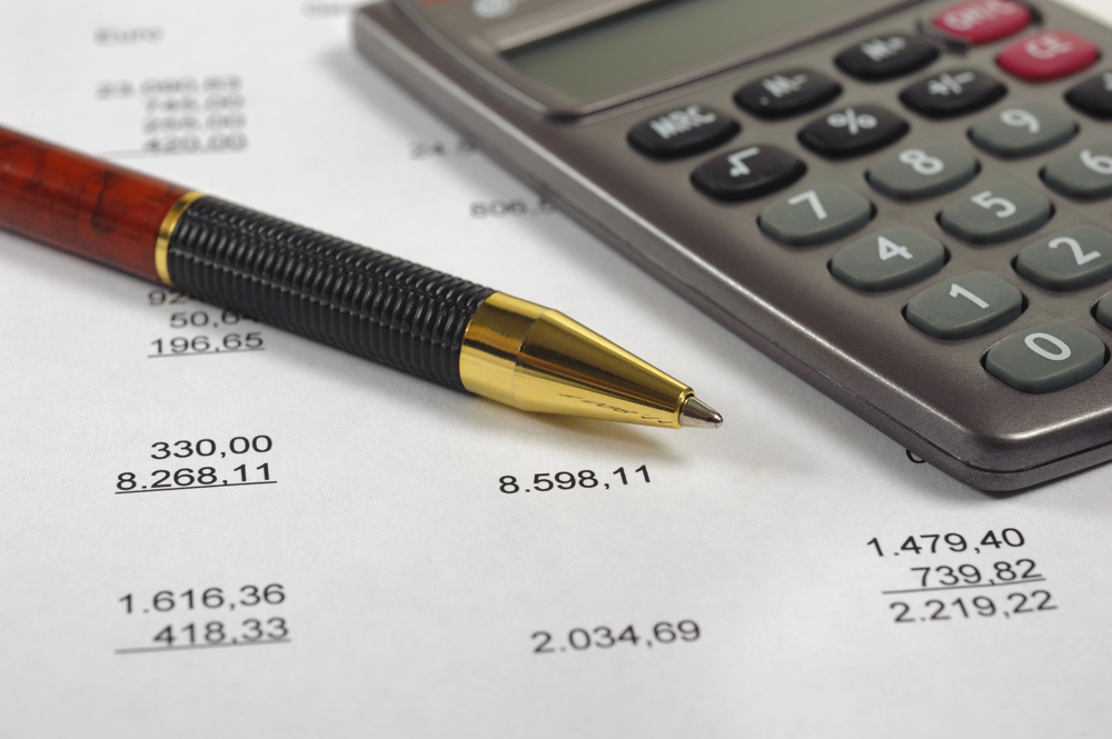 A pen and a calculator resting on a document with columns of financial figures.