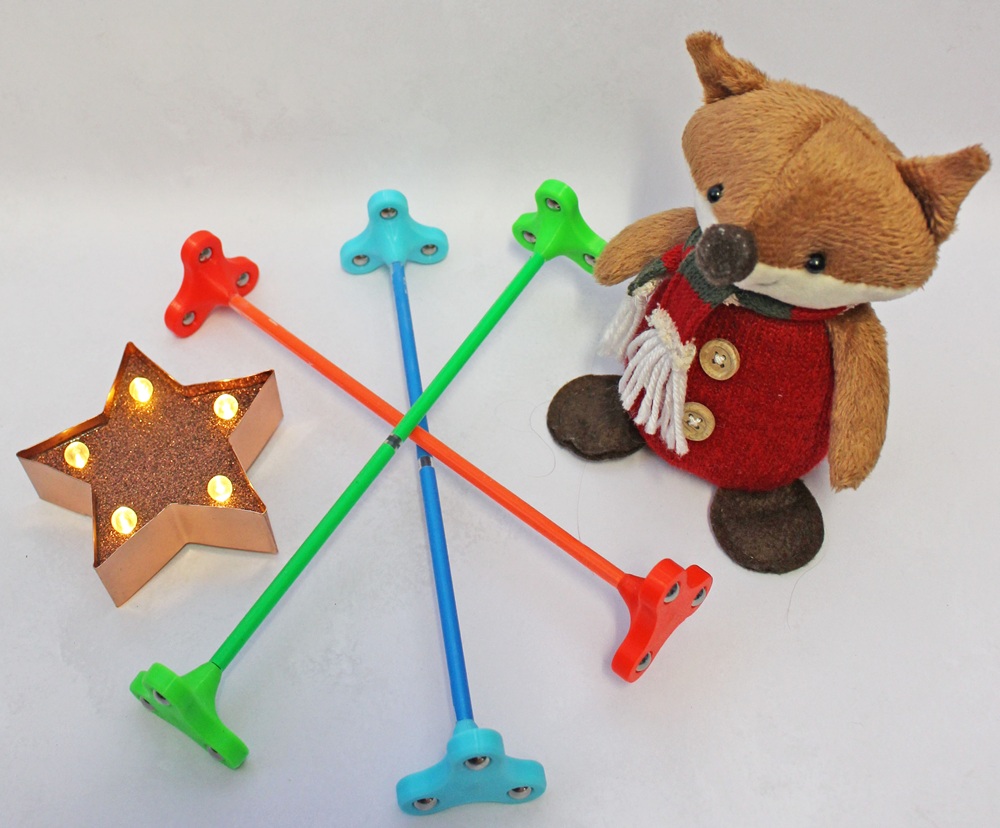 A plush fox toy sits next to a lighted star decoration and three colourful plastic sticks with three-pronged ends.