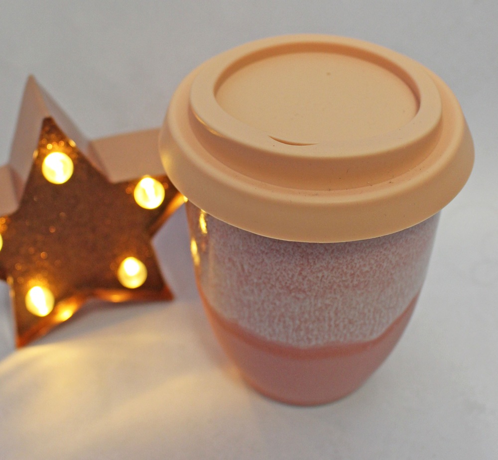 A pink two-toned ceramic travel mug with a peach-coloured lid next to a glowing, star-shaped light.