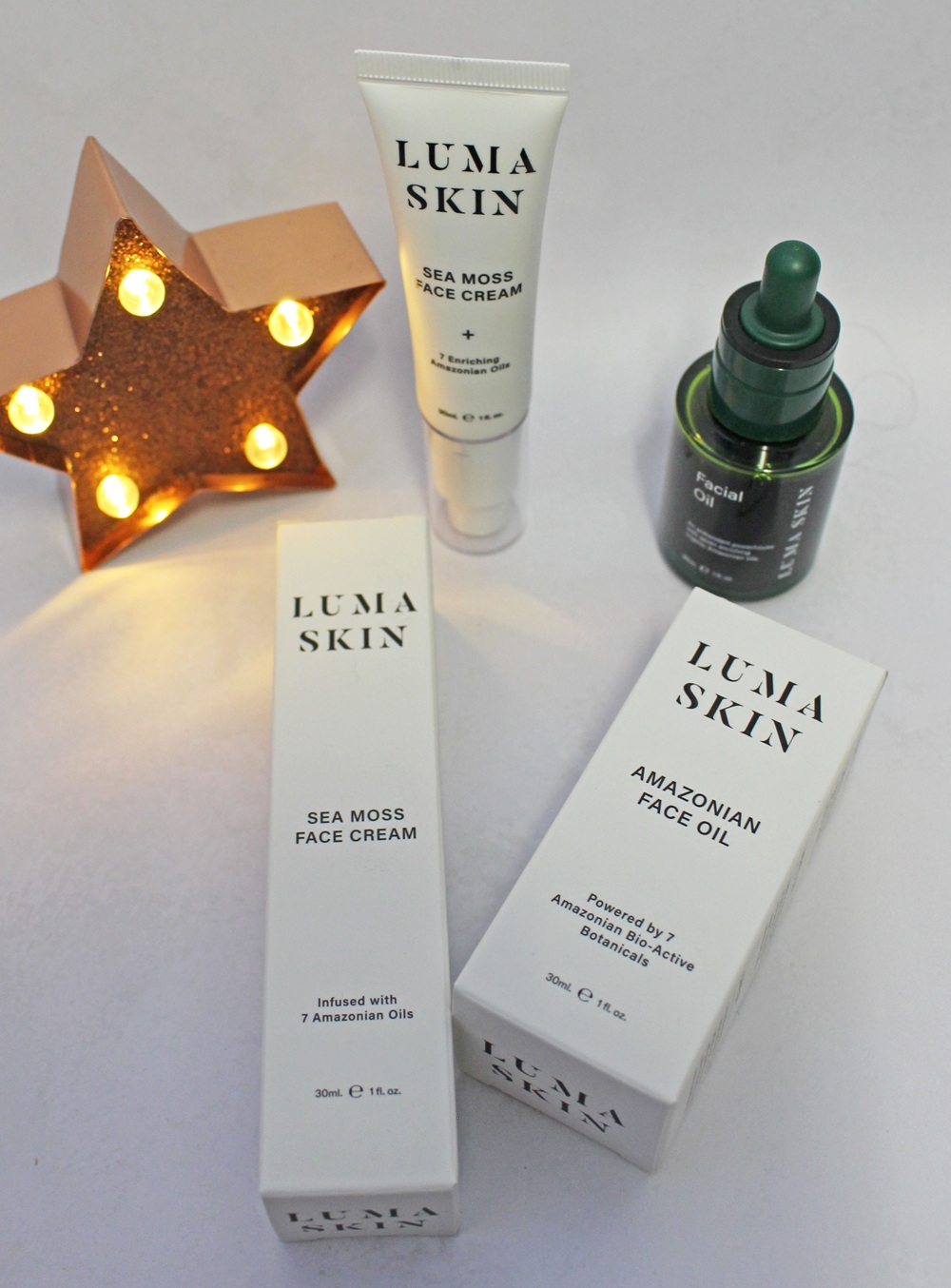 Luma Skin Sea Moss face cream tube and Amazonian face oil dropper bottle, with their respective product boxes and a lit star-shaped ornament.