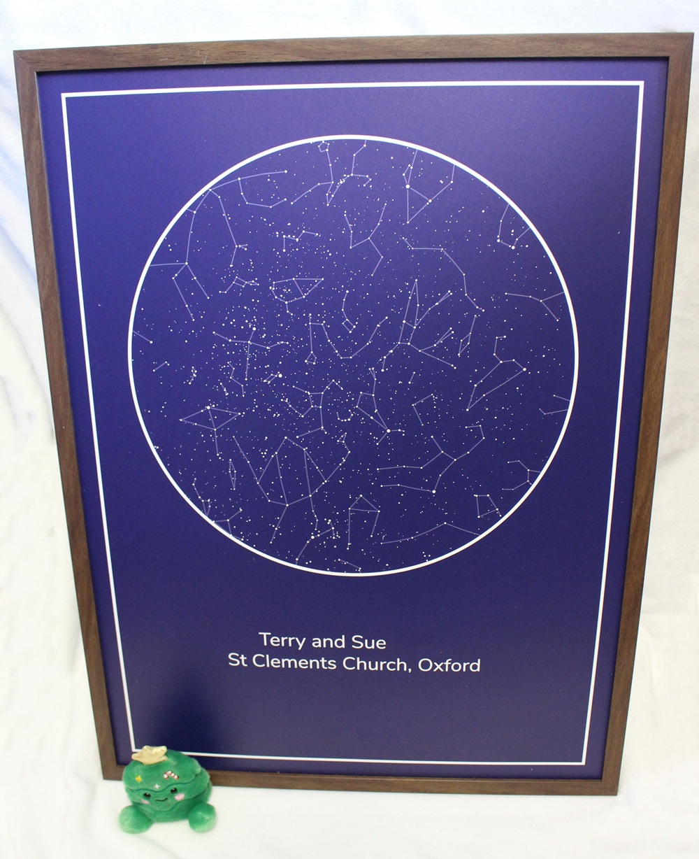 Framed star map print showing the night sky, labelled Terry and Sue, St Clements Church, Oxford, with a small plush Christmas tree toy in the foreground.