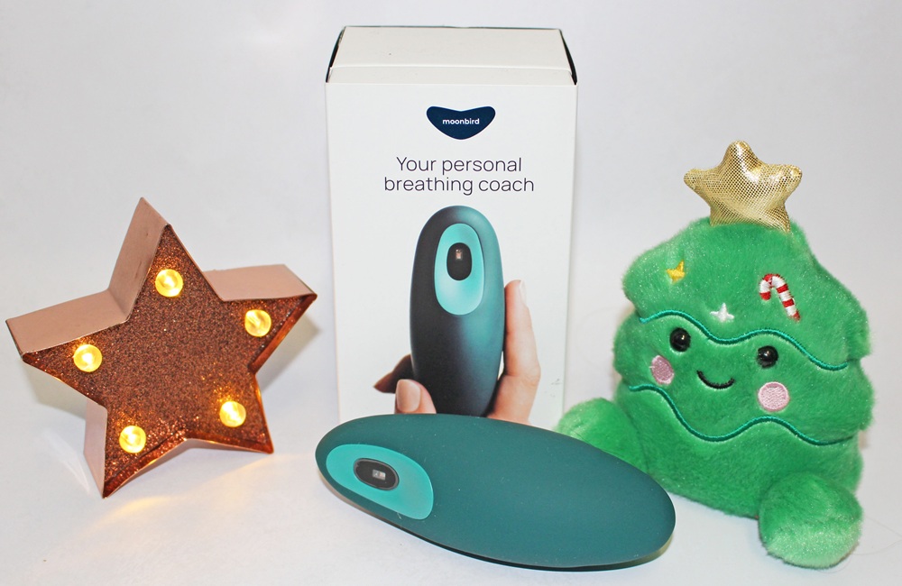 A Moonbird breathing device sits in front of its product box, flanked by a glowing copper star lamp and a plush Christmas tree toy.
