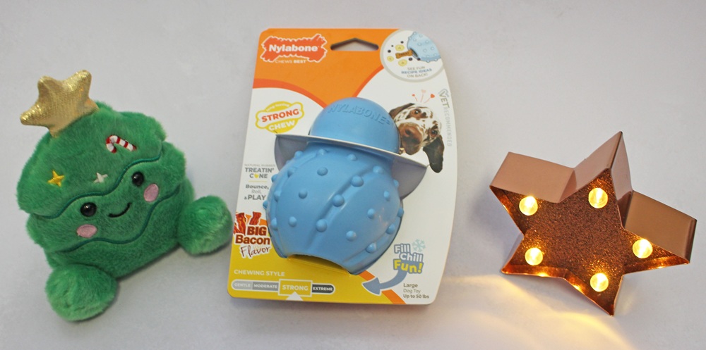 A green plush Christmas tree toy, a blue Nylabone cone-shaped dog chew toy in its original packaging, and a light-up copper-coloured star decoration.