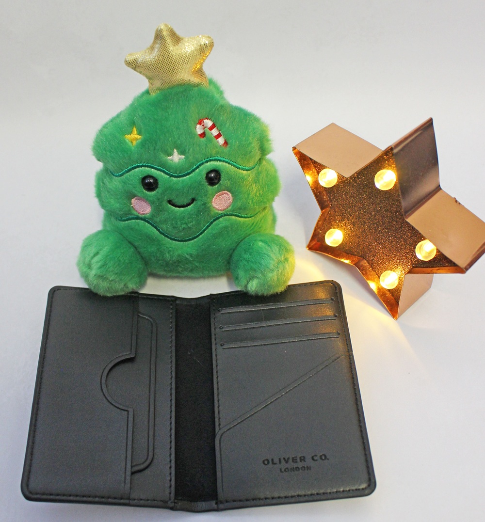 An open black Oliver Co. London wallet sitting next to a plush Christmas tree toy and a lit star decoration.